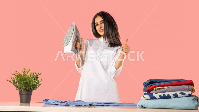 Portrait of an Arab woman holding an electric iron, expressions of admiration and good services, readiness to iron clothes on an ironing board, ironing and organizing clothes, routine household tasks and chores, household electrical appliances, ironing an