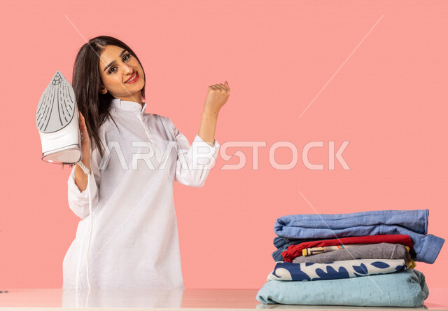 Portrait of an Arab woman, holding an electric iron in her hand, expressions indicating willingness to iron clothes on an ironing board, ironing and organizing clothes, routine household tasks and chores, home electrical appliances, the concept of ironing