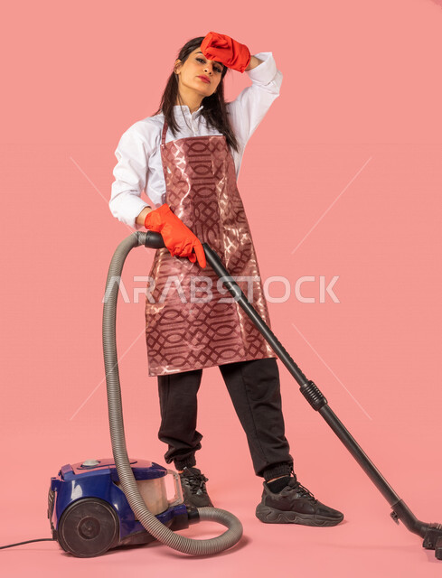 Portrait of an Arab woman wearing gloves and an apron, using a vacuum ...