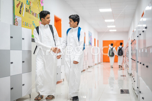 Two Saudi Arabian Gulf students shaking hands, acquaintance and friendship, interdependent relationships, love and interdependence, meeting and communication, smiling face gestures, walking in school corridors, back to school, education in the Kingdom of 