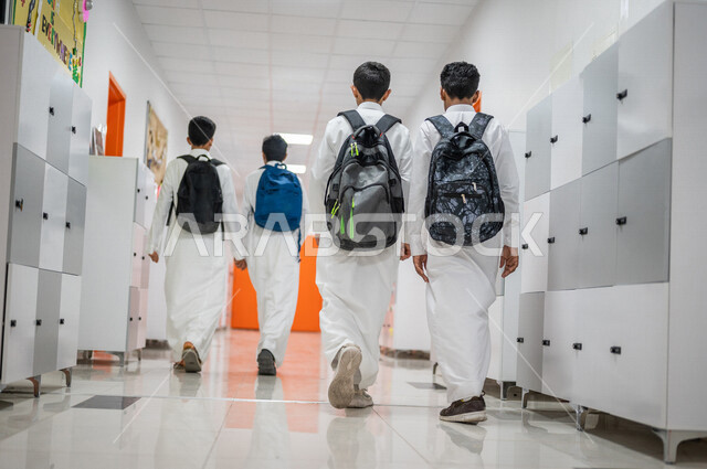 A picture from the back of a group of Saudi Gulf Arab students wandering around the school, walking in the school corridors, back to school, education in the Kingdom of Saudi Arabia