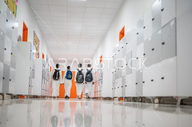 صورة من الخلف لمجموعة من الطلاب العرب الخليجيين السعوديين يتجولون داخل المدرسة، المشي في ممرات المدرسة، العودة إلى المدارس، التعليم في المملكة العربية السعودية