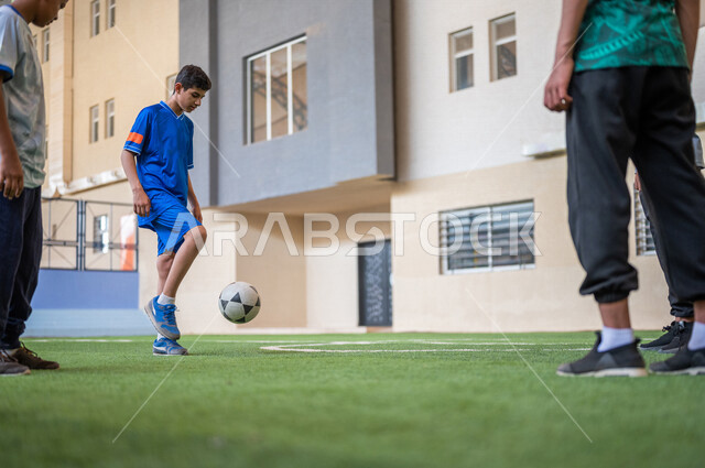 Saudi Gulf Arab students playing football in the school playground, exercising, playing football, dribbling and controlling the ball, physical education class, education in the Kingdom of Saudi Arabia
