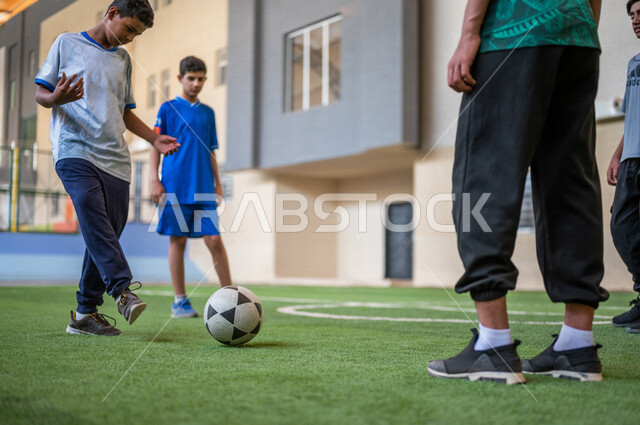 Saudi Gulf Arab students playing football in the school playground, exercising, playing football, dribbling and controlling the ball, physical education class, education in the Kingdom of Saudi Arabia