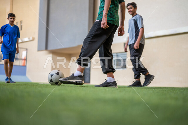 Saudi Gulf Arab students playing football in the school playground, exercising, playing football, dribbling and controlling the ball, physical education class, education in the Kingdom of Saudi Arabia