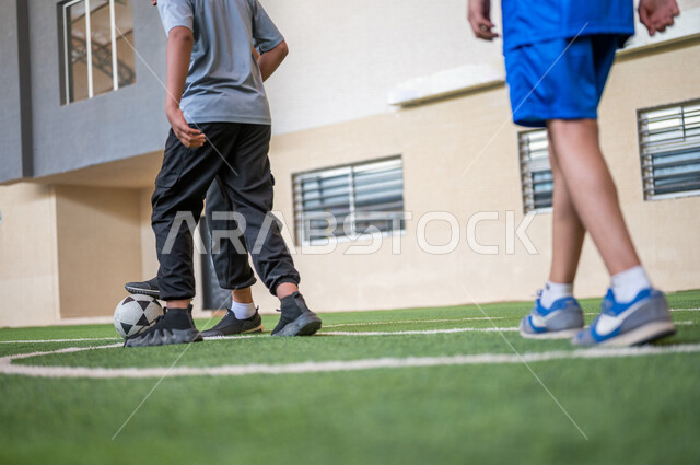 طلاب عرب خليجيين سعوديين يلعبون كرة القدم في ملعب المدرسة، ممارسة التمارين الرياضية، لعب كرة القدم، المراوغة والتحكم بالكرة، حصة التربية الرياضية، التعليم في المملكة العربية السعودية