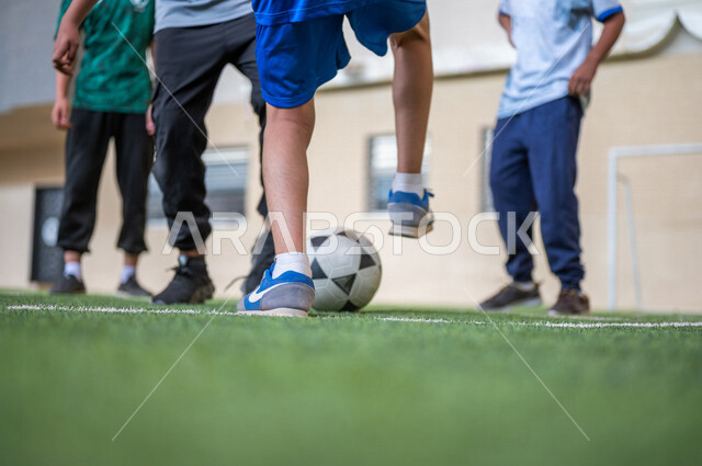 Saudi Gulf Arab students playing football in the school playground, exercising, playing football, dribbling and controlling the ball, physical education class, education in the Kingdom of Saudi Arabia