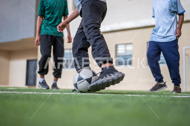 طلاب عرب خليجيين سعوديين يلعبون كرة القدم في ملعب المدرسة، ممارسة التمارين الرياضية، لعب كرة القدم، المراوغة والتحكم بالكرة، حصة التربية الرياضية، التعليم في المملكة العربية السعودية