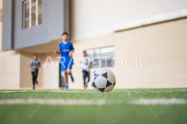 طلاب عرب خليجيين سعوديين يلعبون كرة القدم في ملعب المدرسة، ممارسة التمارين الرياضية، لعب كرة القدم، المراوغة والتحكم بالكرة، حصة التربية الرياضية، التعليم في المملكة العربية السعودية