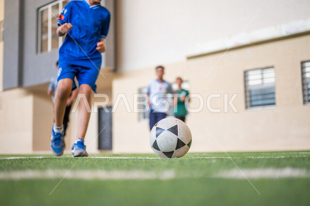طلاب عرب خليجيين سعوديين يلعبون كرة القدم في ملعب المدرسة، ممارسة التمارين الرياضية، لعب كرة القدم، المراوغة والتحكم بالكرة، حصة التربية الرياضية، التعليم في المملكة العربية السعودية