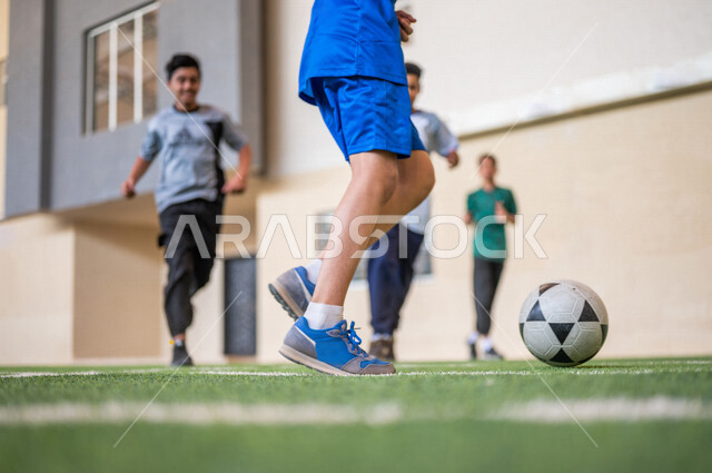 طلاب عرب خليجيين سعوديين يلعبون كرة القدم في ملعب المدرسة، ممارسة التمارين الرياضية، لعب كرة القدم، المراوغة والتحكم بالكرة، حصة التربية الرياضية، التعليم في المملكة العربية السعودية