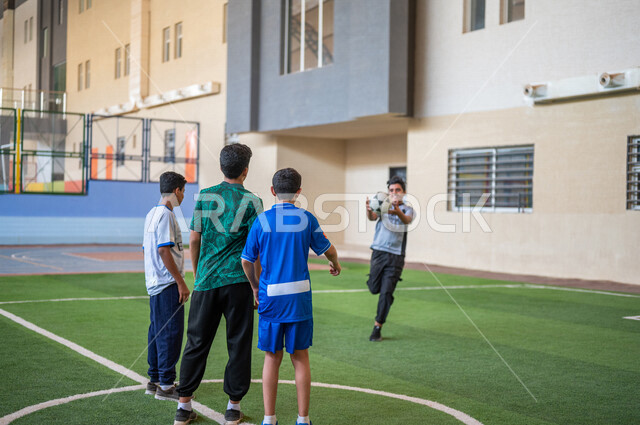 طلاب عرب خليجيين سعوديين يلعبون كرة القدم في ملعب المدرسة، ممارسة التمارين الرياضية، لعب كرة القدم، حصة التربية الرياضية، التعليم في المملكة العربية السعودية
