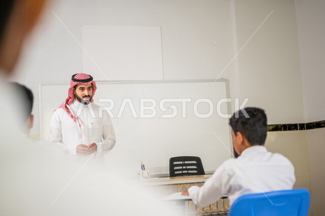 معلم عربي خليجي سعودي يقوم بشرح الدرس للطلاب، لوحة مدرسية بيضاء، المشاركة الفعالة للطلاب، التعليم الفعال، أهداف التربية والتعليم، التفاعل والمشاركة داخل الفصل الدراسي، التعليم في المملكة العربية السعودية