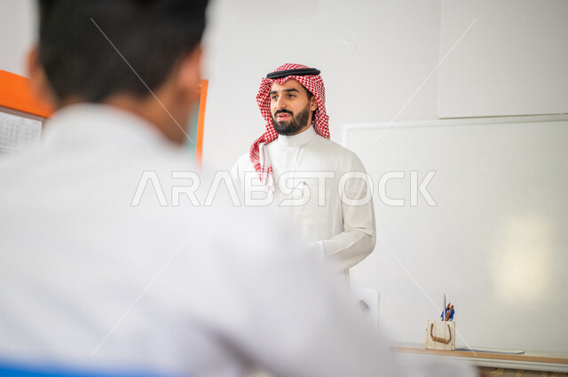 معلم عربي خليجي سعودي يقوم بشرح الدرس للطلاب، لوحة مدرسية بيضاء، المشاركة الفعالة للطلاب، التعليم الفعال، أهداف التربية والتعليم، التفاعل والمشاركة داخل الفصل الدراسي، التعليم في المملكة العربية السعودية
