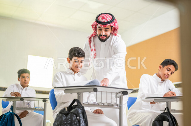 A close-up of a Saudi Arab Gulf student with facial gestures indicating confusion, a teacher helping the student to solve the lesson questions, the active participation of students, effective education, the goals of education, education in Saudi Arabia