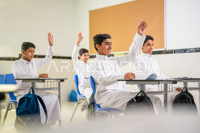 مجموعة من الطلاب العرب الخليجيين السعوديين يتفاعلون في الحصة الدراسية من خلال رفع ايديهم للاجابة على اسئلة المدرس، المشاركة الفعالة للطلاب، التعليم الفعال، أهداف التربية والتعليم، التفاعل والمشاركة داخل الفصل الدراسي، التعليم في السعودية