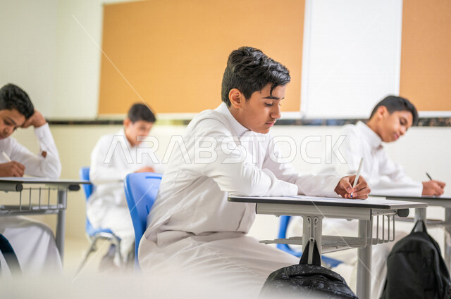 معلم عربي خليجي سعودي يقوم بتوزيع أوراق الاختبارات، طلاب يقومون بحل أسئلة الاختبارات، مراقبة الطلاب اثناء تقديم الاختبارات،  أهداف التربية والتعليم، اختبارات نهائية، نهاية الفصل الدراسي، التعليم في المملكة العربية السعودية