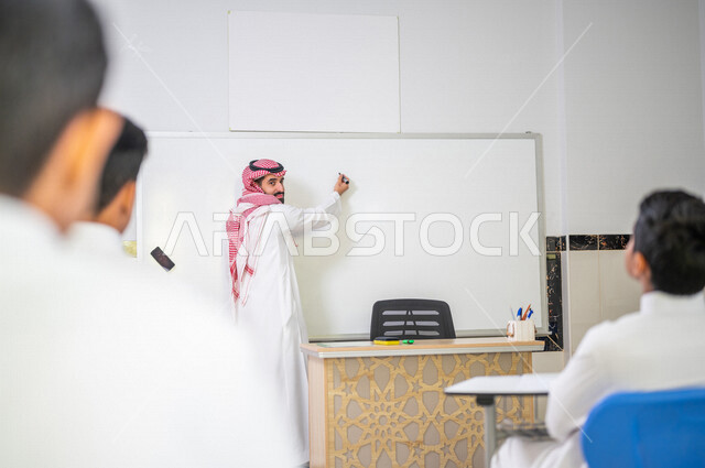 معلم عربي خليجي سعودي يقوم بشرح الدرس الدرس للطلاب، استخدام اللوحة المدرسية البيضاء، المشاركة الفعالة للطلاب، التعليم الفعال، أهداف التربية والتعليم، التفاعل والمشاركة داخل الفصل الدراسي، التعليم في السعودية