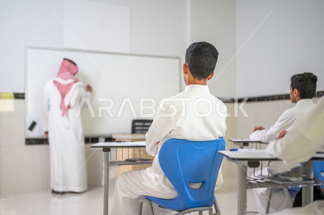 معلم عربي خليجي سعودي يقوم بشرح الدرس الدرس للطلاب، استخدام اللوحة المدرسية البيضاء، المشاركة الفعالة للطلاب، التعليم الفعال، أهداف التربية والتعليم، التفاعل والمشاركة داخل الفصل الدراسي، التعليم في السعودية