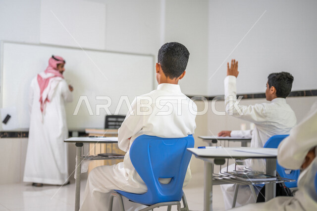 معلم عربي خليجي سعودي يقوم بشرح الدرس، طالب يتفاعل في الحصة الدراسية من خلال رفع يده للاجابة على اسئلة المدرس، المشاركة الفعالة للطلاب، أهداف التربية والتعليم، التفاعل والمشاركة داخل الفصل الدراسي، التعليم في السعودية