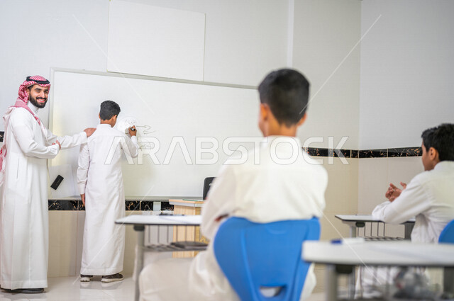 A Saudi Gulf Arab teacher explains the lesson to the students, the use of the white school board, the active participation of students, effective teaching, the goals of education, interaction and participation in the classroom, education in Saudi Arabia