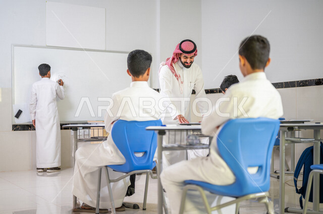 معلم عربي خليجي سعودي يقوم بشرح الدرس الدرس للطلاب، استخدام اللوحة المدرسية البيضاء، المشاركة الفعالة للطلاب، التعليم الفعال، أهداف التربية والتعليم، التفاعل والمشاركة داخل الفصل الدراسي، التعليم في السعودية
