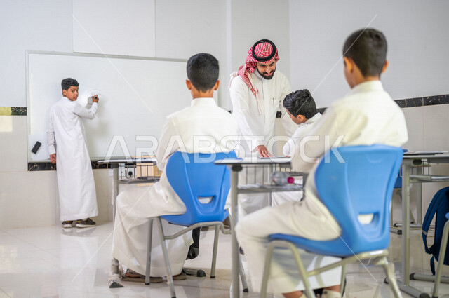 معلم عربي خليجي سعودي يقوم بشرح الدرس الدرس للطلاب، استخدام اللوحة المدرسية البيضاء، المشاركة الفعالة للطلاب، التعليم الفعال، أهداف التربية والتعليم، التفاعل والمشاركة داخل الفصل الدراسي، التعليم في السعودية