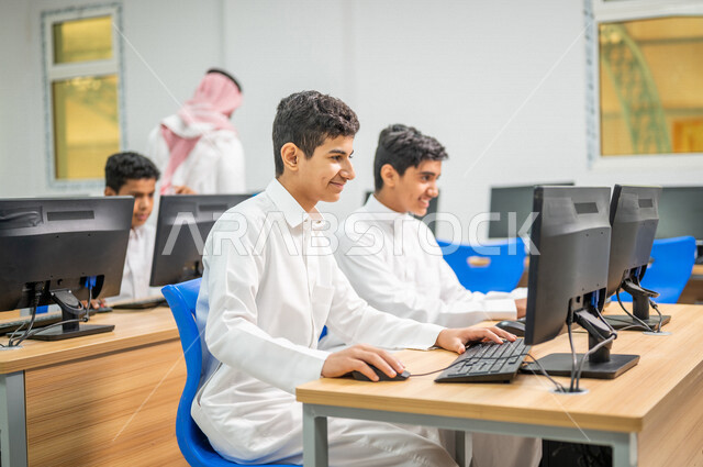 معلم عربي خليجي سعودي في معمل الحاسب الآلي، تعليم الطلبة كيفية استخدام الكمبيوتر في المدرسة، استخدام لوحة المفاتيح للكتابة، التعليم الالكتروني، المناهج المطورة، المشاركة الفعالة للطلاب، التعليم الفعال، التعليم في المملكة العربية السعودية