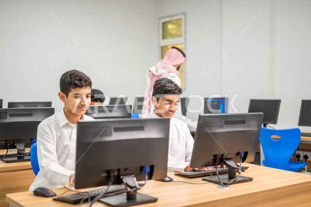معلم عربي خليجي سعودي في معمل الحاسب الآلي، تعليم الطلبة كيفية استخدام الكمبيوتر في المدرسة، استخدام لوحة المفاتيح للكتابة، التعليم الالكتروني، المناهج المطورة، المشاركة الفعالة للطلاب، التعليم الفعال، التعليم في المملكة العربية السعودية