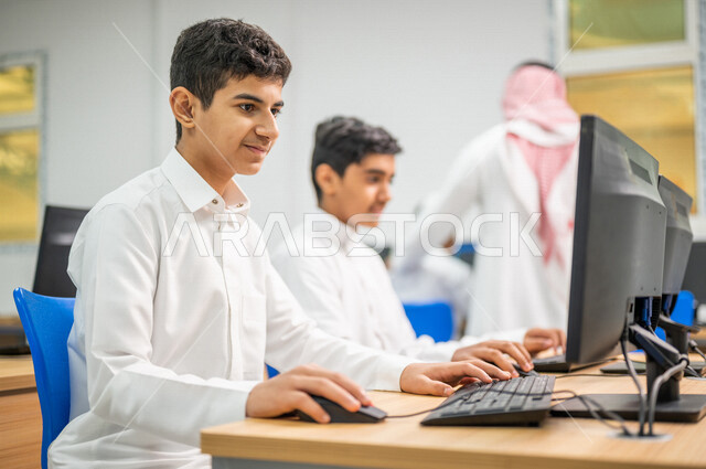 معلم عربي خليجي سعودي في معمل الحاسب الآلي، تعليم الطلبة كيفية استخدام الكمبيوتر في المدرسة، استخدام لوحة المفاتيح للكتابة، التعليم الالكتروني، المناهج المطورة، المشاركة الفعالة للطلاب، التعليم الفعال، التعليم في المملكة العربية السعودية