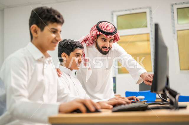 معلم عربي خليجي سعودي في معمل الحاسب الآلي، تعليم الطلبة كيفية استخدام الكمبيوتر في المدرسة، استخدام لوحة المفاتيح للكتابة، التعليم الالكتروني، المناهج المطورة، المشاركة الفعالة للطلاب، التعليم الفعال، التعليم في المملكة العربية السعودية