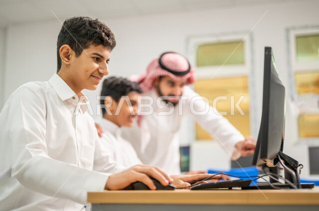 معلم عربي خليجي سعودي في معمل الحاسب الآلي، تعليم الطلبة كيفية استخدام الكمبيوتر في المدرسة، استخدام لوحة المفاتيح للكتابة، التعليم الالكتروني، المناهج المطورة، المشاركة الفعالة للطلاب، التعليم الفعال، التعليم في المملكة العربية السعودية