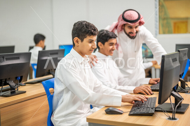 معلم عربي خليجي سعودي في معمل الحاسب الآلي، تعليم الطلبة كيفية استخدام الكمبيوتر في المدرسة، استخدام لوحة المفاتيح للكتابة، التعليم الالكتروني، المناهج المطورة، المشاركة الفعالة للطلاب، التعليم الفعال، التعليم في المملكة العربية السعودية