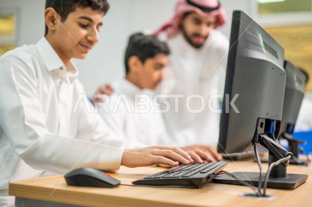 صورة مقربة لمعلم عربي خليجي سعودي في معمل الحاسب الآلي، تعليم الطلبة كيفية استخدام الكمبيوتر في المدرسة، استخدام لوحة المفاتيح للكتابة، التعليم الالكتروني، المناهج المطورة، المشاركة الفعالة للطلاب، التعليم الفعال، التعليم في المملكة العربية السعودية