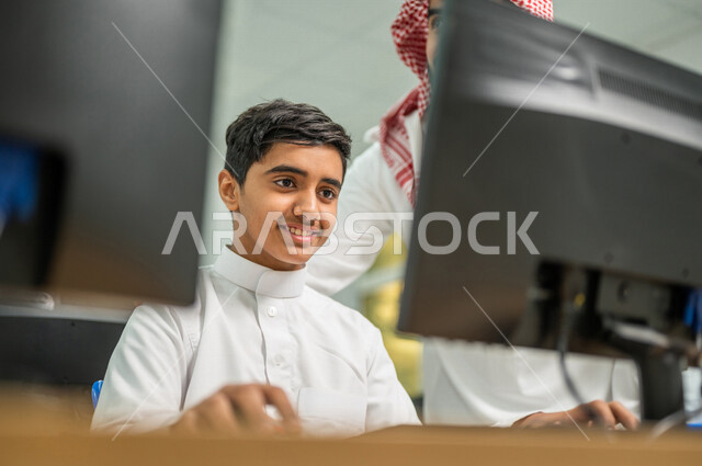 صورة مقربة لمعلم عربي خليجي سعودي في معمل الحاسب الآلي، تعليم الطلبة كيفية استخدام الكمبيوتر في المدرسة، استخدام لوحة المفاتيح للكتابة، التعليم الالكتروني، المناهج المطورة، المشاركة الفعالة للطلاب، التعليم الفعال، التعليم في المملكة العربية السعودية