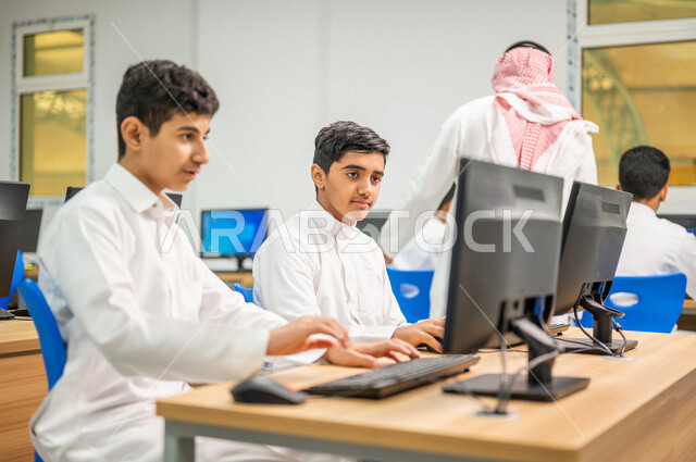 Saudi Arab Gulf teacher in the computer lab, teaching students how to use a computer in school, using the keyboard to write, e-learning, developed curricula, active participation of students, effective education, education in the Kingdom of Saudi Arabia