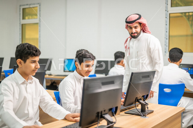 معلم عربي خليجي سعودي في معمل الحاسب الآلي، تعليم الطلبة كيفية استخدام الكمبيوتر في المدرسة، استخدام لوحة المفاتيح للكتابة، التعليم الالكتروني، المناهج المطورة، المشاركة الفعالة للطلاب، التعليم الفعال، التعليم في المملكة العربية السعودية