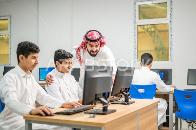 معلم عربي خليجي سعودي في معمل الحاسب الآلي، تعليم الطلبة كيفية استخدام الكمبيوتر في المدرسة، استخدام لوحة المفاتيح للكتابة، التعليم الالكتروني، المناهج المطورة، المشاركة الفعالة للطلاب، التعليم الفعال، التعليم في المملكة العربية السعودية