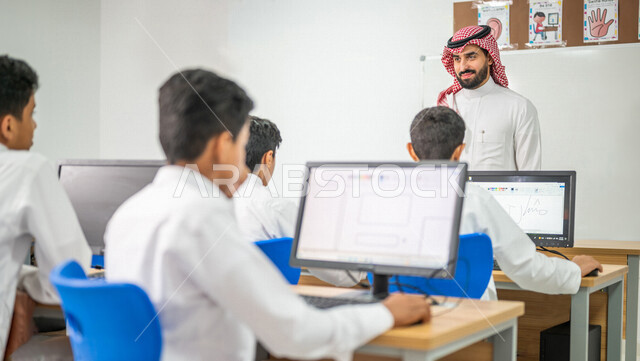 معلم عربي خليجي سعودي في معمل الحاسب الآلي، تعليم الطلبة كيفية استخدام الكمبيوتر في المدرسة، استخدام لوحة المفاتيح للكتابة، التعليم الالكتروني، المناهج المطورة، المشاركة الفعالة للطلاب، التعليم الفعال، التعليم في المملكة العربية السعودية