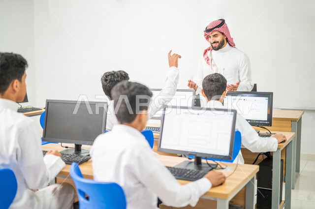 معلم عربي خليجي سعودي في معمل الحاسب الآلي، تعليم الطلبة كيفية استخدام الكمبيوتر في المدرسة، استخدام لوحة المفاتيح للكتابة، التعليم الالكتروني، المناهج المطورة، المشاركة الفعالة للطلاب، التعليم الفعال، التعليم في المملكة العربية السعودية