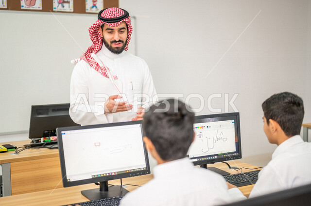 A close-up of a Saudi Arabian Gulf teacher in the computer lab, teaching students how to use a computer in school, using the keyboard to write, e-learning, developed curricula, active participation of students, effective education, education in the Kingdo