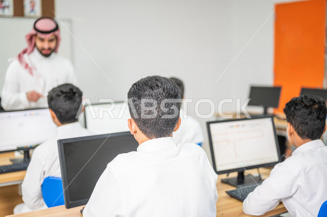 معلم عربي خليجي سعودي في معمل الحاسب الآلي، تعليم الطلبة كيفية استخدام الكمبيوتر في المدرسة، استخدام لوحة المفاتيح للكتابة، التعليم الالكتروني، المناهج المطورة، المشاركة الفعالة للطلاب، التعليم الفعال، التعليم في المملكة العربية السعودية