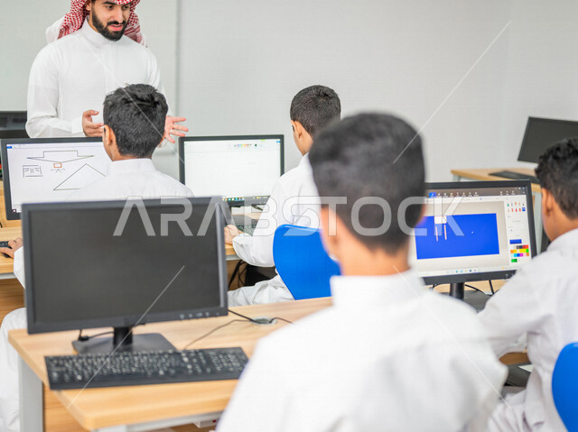 معلم عربي خليجي سعودي في معمل الحاسب الآلي، تعليم الطلبة كيفية استخدام الكمبيوتر في المدرسة، استخدام لوحة المفاتيح للكتابة، التعليم الالكتروني، المناهج المطورة، المشاركة الفعالة للطلاب، التعليم الفعال، التعليم في المملكة العربية السعودية