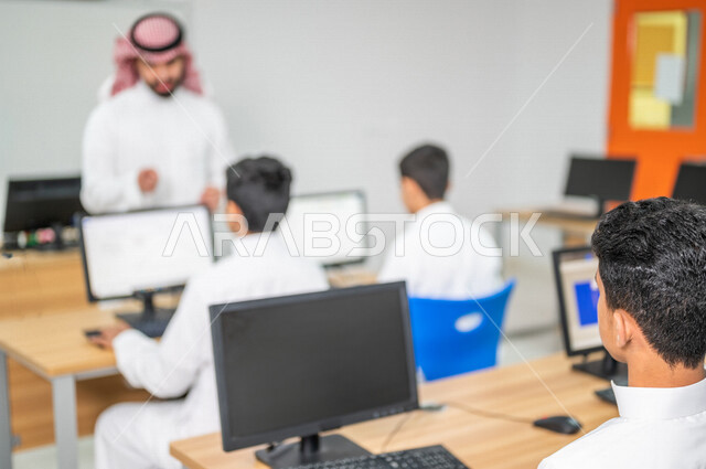 معلم عربي خليجي سعودي في معمل الحاسب الآلي، تعليم الطلبة كيفية استخدام الكمبيوتر في المدرسة، استخدام لوحة المفاتيح للكتابة، التعليم الالكتروني، المناهج المطورة، المشاركة الفعالة للطلاب، التعليم الفعال، التعليم في المملكة العربية السعودية