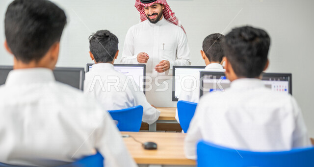 معلم عربي خليجي سعودي في معمل الحاسب الآلي، تعليم الطلبة كيفية استخدام الكمبيوتر في المدرسة، استخدام لوحة المفاتيح للكتابة، التعليم الالكتروني، المناهج المطورة، المشاركة الفعالة للطلاب، التعليم الفعال، التعليم في المملكة العربية السعودية
