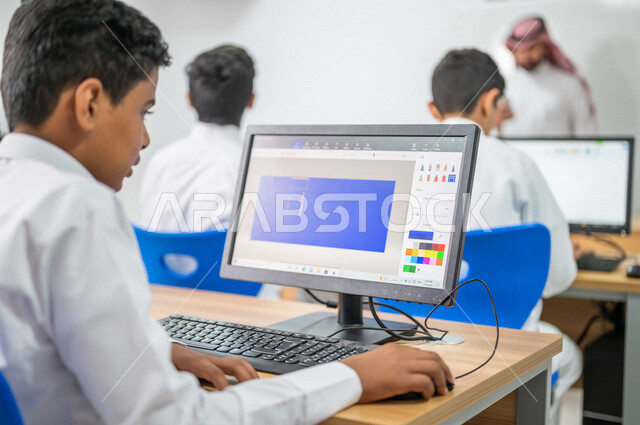 معلم عربي خليجي سعودي في معمل الحاسب الآلي، تعليم الطلبة كيفية استخدام الكمبيوتر في المدرسة، استخدام لوحة المفاتيح للكتابة، التعليم الالكتروني، المناهج المطورة، المشاركة الفعالة للطلاب، التعليم الفعال، التعليم في المملكة العربية السعودية