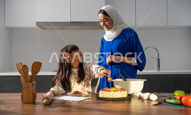 أم عربيه سعوديه خليجيه تشارك ابنتها في اعداد الحلوى في المطبخ، الوقوف أمام طاولة المطبخ, مقادير صنع الكعك, مشاركة البنات في الأعمال المنزلية، الإستمتاع في صنع الكعك، تعليم فنون الطبخ, الشيف الصغير