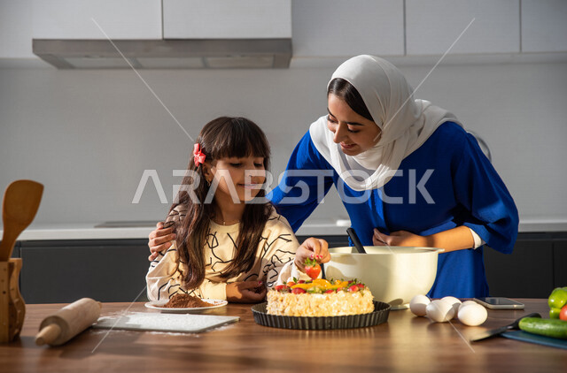 أم عربيه سعوديه خليجيه تشارك ابنتها في اعداد الحلوى في المطبخ، الوقوف أمام طاولة المطبخ, مقادير صنع الكعك, مشاركة البنات في الأعمال المنزلية، الإستمتاع في صنع الكعك، تعليم فنون الطبخ, الشيف الصغير