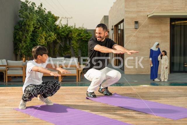 رجل سعودي خليجي يمارس الرياضة الصباحية في فناء المنزل بمشاركة ابنه الصغير ،اليوغا و الاسترخاء ، ممارسة الرياضة الصباحية ، نشاط بدني  للمحافظة على اللياقة و الصحة الجيدة ، ممارسة التمارين الرياضية 