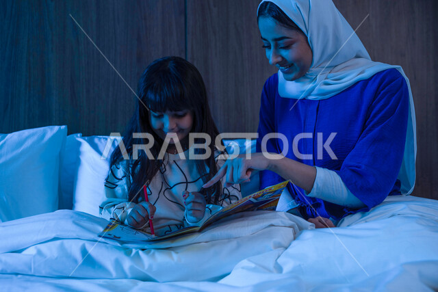 صوره مقربه لأم عربية خليجية سعودية تجلس مع إبنتها على السرير، قضاء وقت ممتع قبل النوم، تربية الأبناء، مفهوم الترابط الأسري، حنان الأم على الأطفال, قراءة القصص قبل النوم